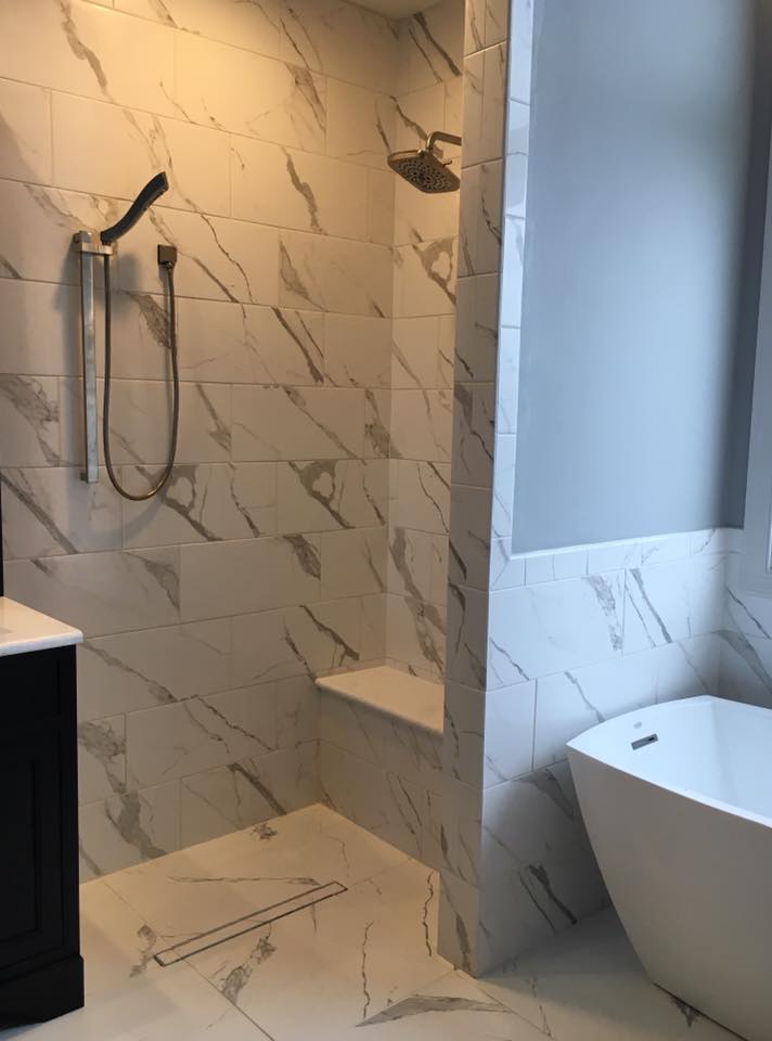 Marble-look tiled shower with built-in bench next to a freestanding tub.