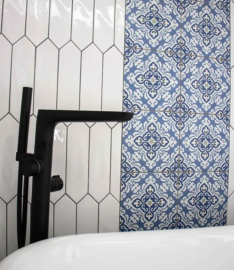 Matte black freestanding bathtub faucet against white and blue patterned tile walls.