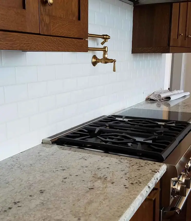 White subway tile kitchen backsplash with a brass pot filler faucet and gas stove.