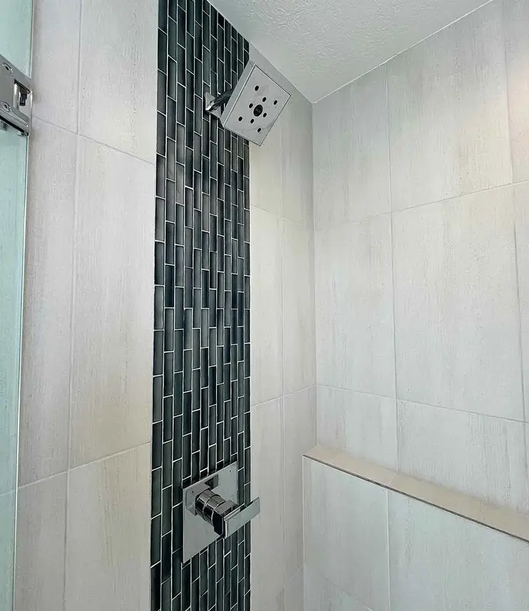 Walk-in shower with light tile walls, a dark vertical accent tile strip, and chrome fixtures.