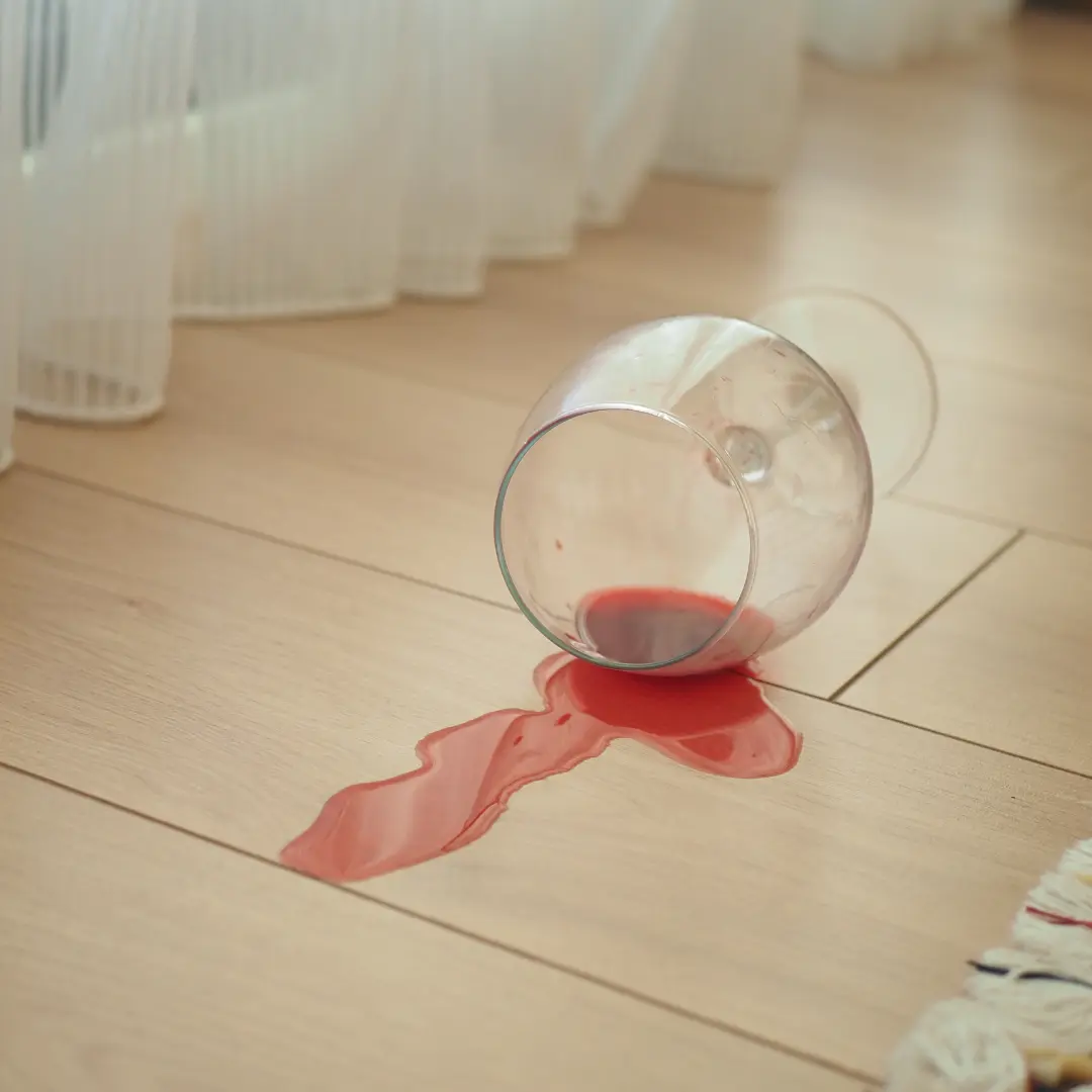 Red wine spilled from a glass on light wood flooring.