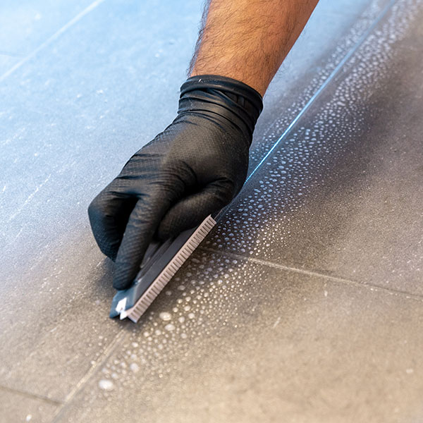 Gloved hand scrubbing tile grout with a small brush.
