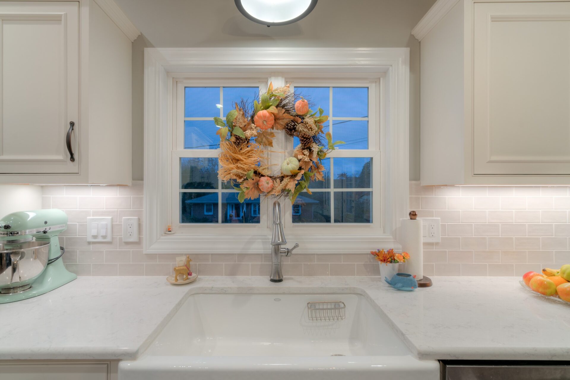White farmhouse kitchen sink with subway tile backsplash and a seasonal window wreath.