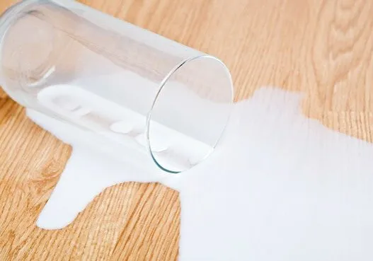 Spilled glass of milk on a light wood floor.