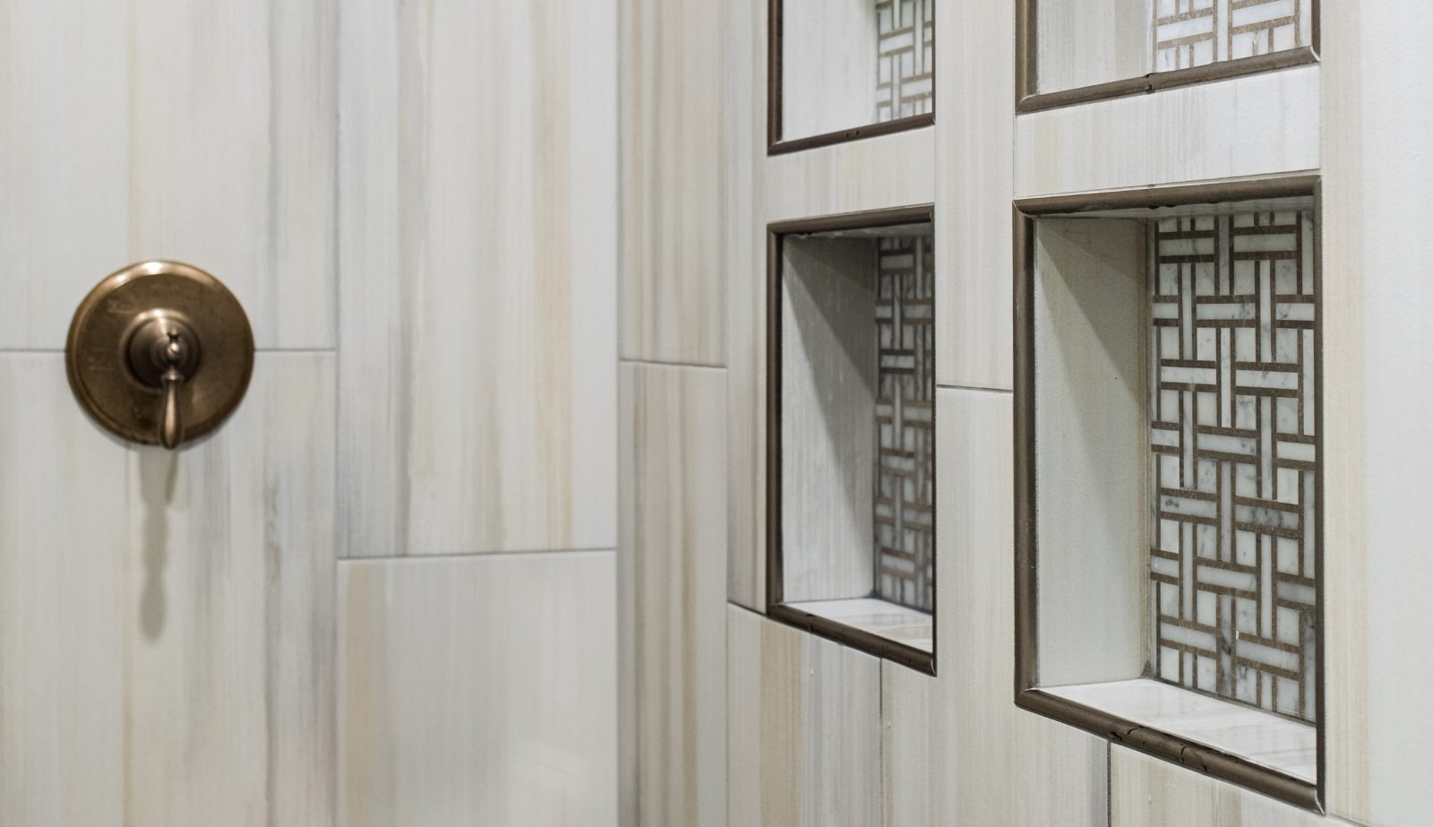 Tiled shower wall featuring bronze fixtures and pattern-lined recessed niches.