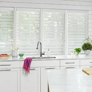 White sheer horizontal shades over a kitchen sink.